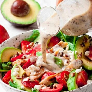 A person pouring a dressing on a strawberry chicken salad.