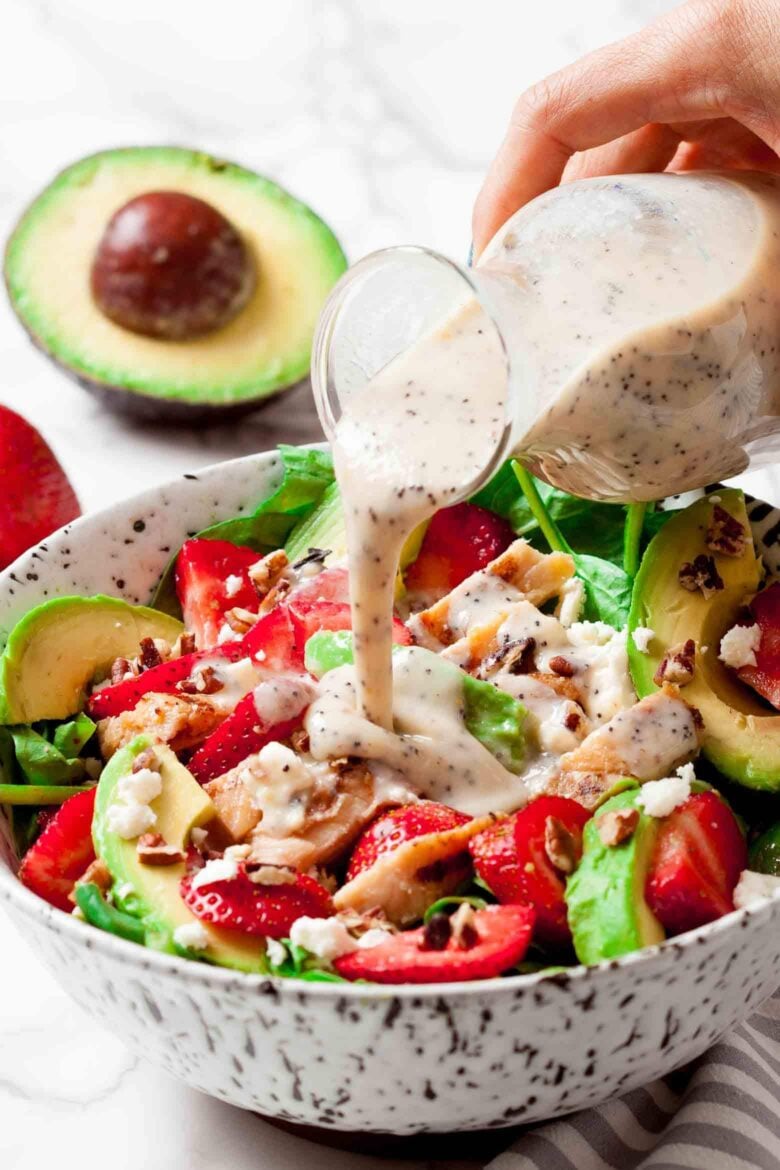 A person pouring a dressing on a strawberry chicken salad.