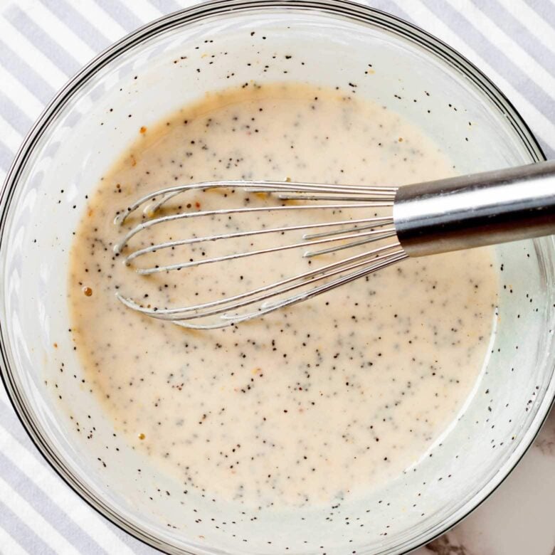 A mixing bowl with poppyseed dressing and a whisk.