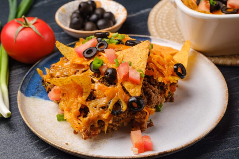 A plate with a serving of taco casserole, garnished with chopped tomatoes, green onions, and black olives.