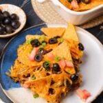 A plate with a serving of taco casserole, garnished with chopped tomatoes, green onions, and black olives.