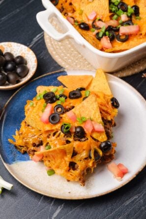 A plate with a serving of taco casserole, garnished with chopped tomatoes, green onions, and black olives.