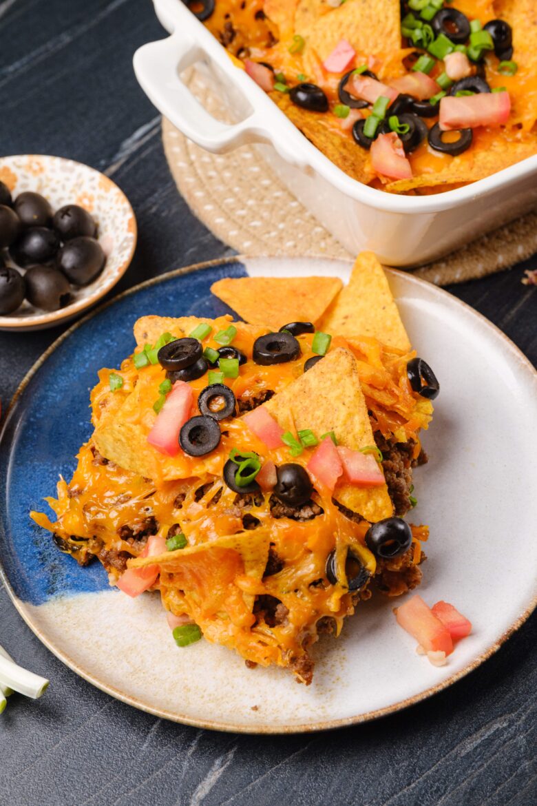 A plate with a serving of taco casserole, garnished with chopped tomatoes, green onions, and black olives.