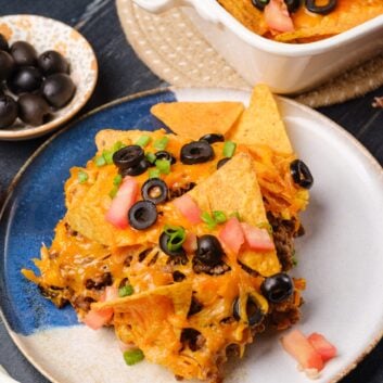 A plate with a serving of taco casserole, garnished with chopped tomatoes, green onions, and black olives.