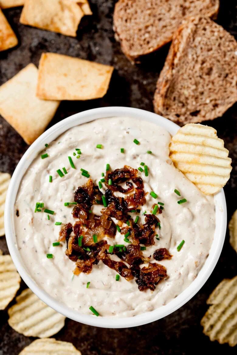 A bowl of caramelized onion dip garnished with caramelized onions and served with chips and crackers.