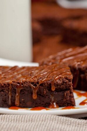 Two fudgy dark chocolate brownies drizzled with salted caramel sauce on a white plate.