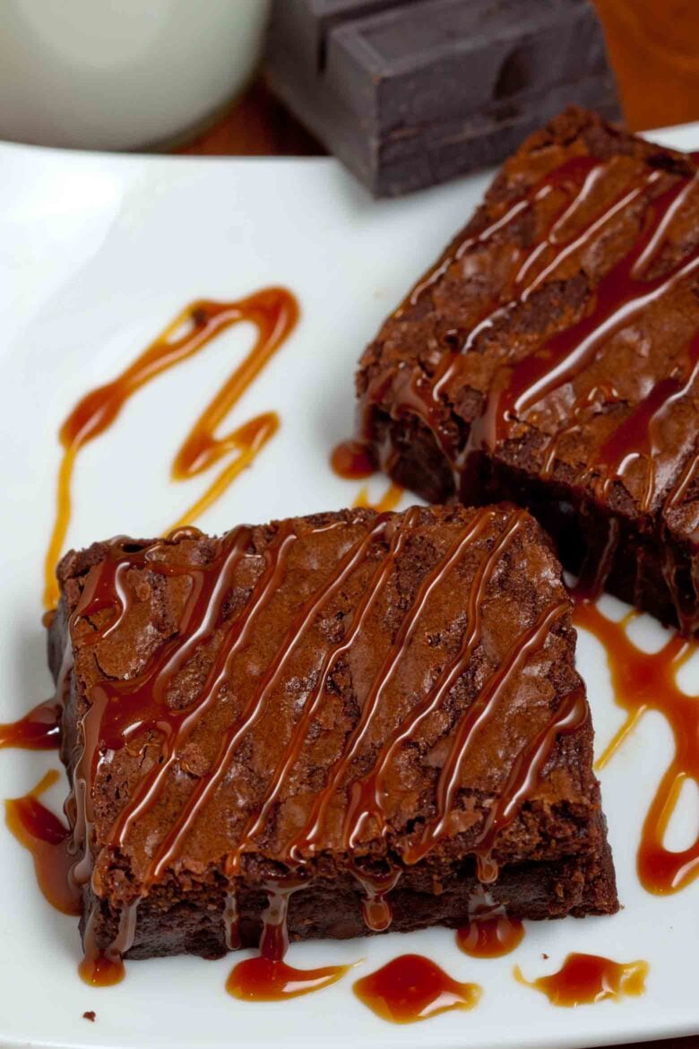 Dark chocolate brownies with caramel drizzle on a white plate.