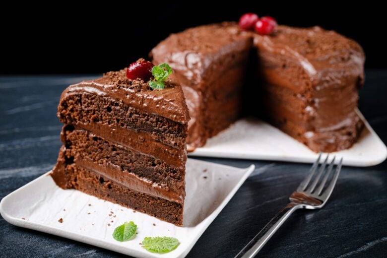 A slice of super moist eggless chocolate cake on a plate with a fork.