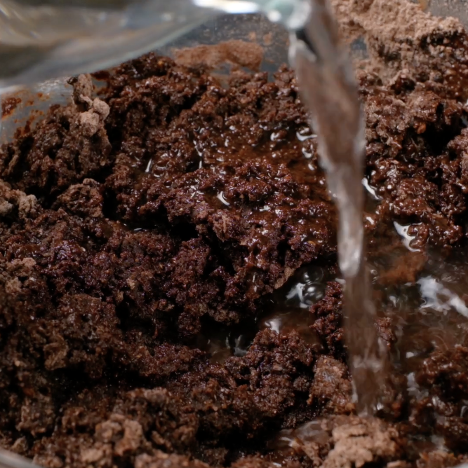 Water being poured into chocolate cake batter in a bowl.