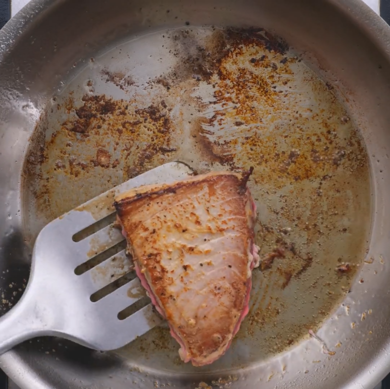 Ahi tuna searing in a pan on second side.