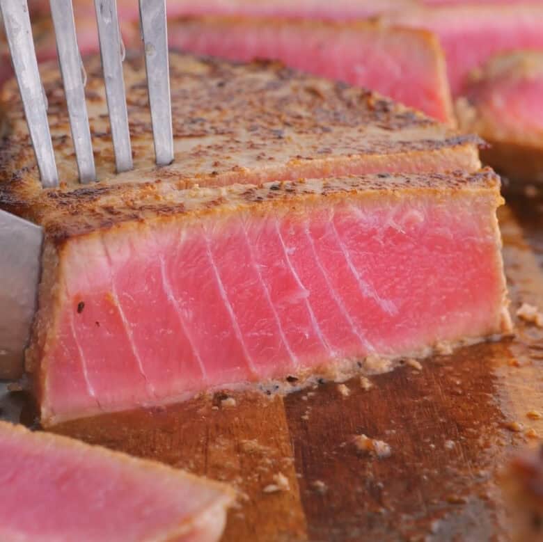 Seared ahi tuna being sliced on a cutting board.