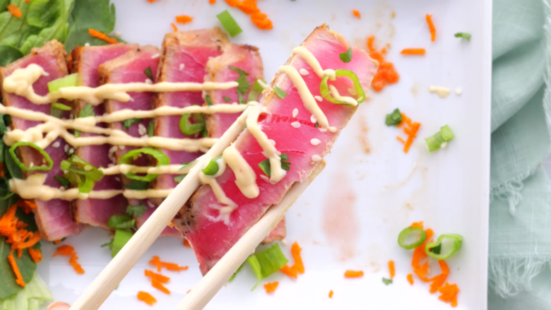 Seared ahi tuna being served on a plate with garnishes.