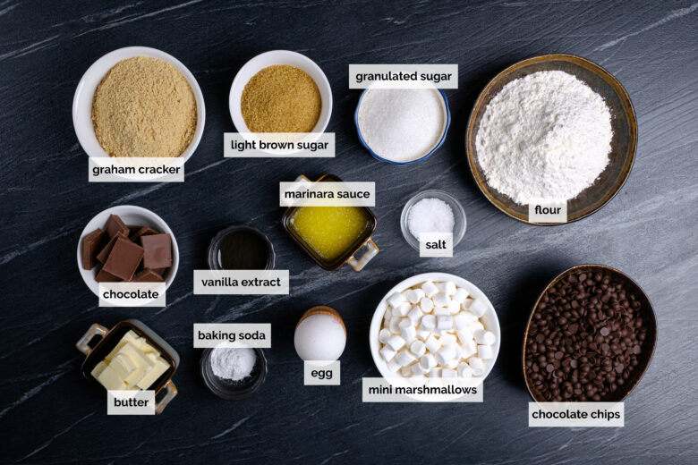 Ingredients to make s'mores cookie bars on a dark surface.