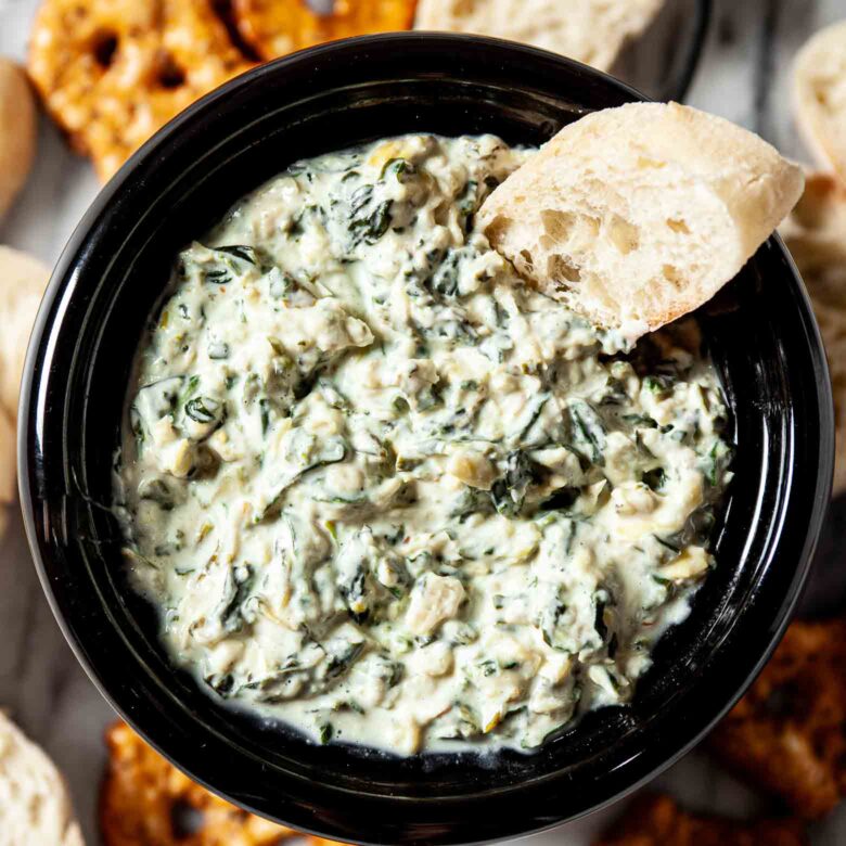 A bowl of crockpot spinach and artichoke dip with pretzels and pretzel sticks.