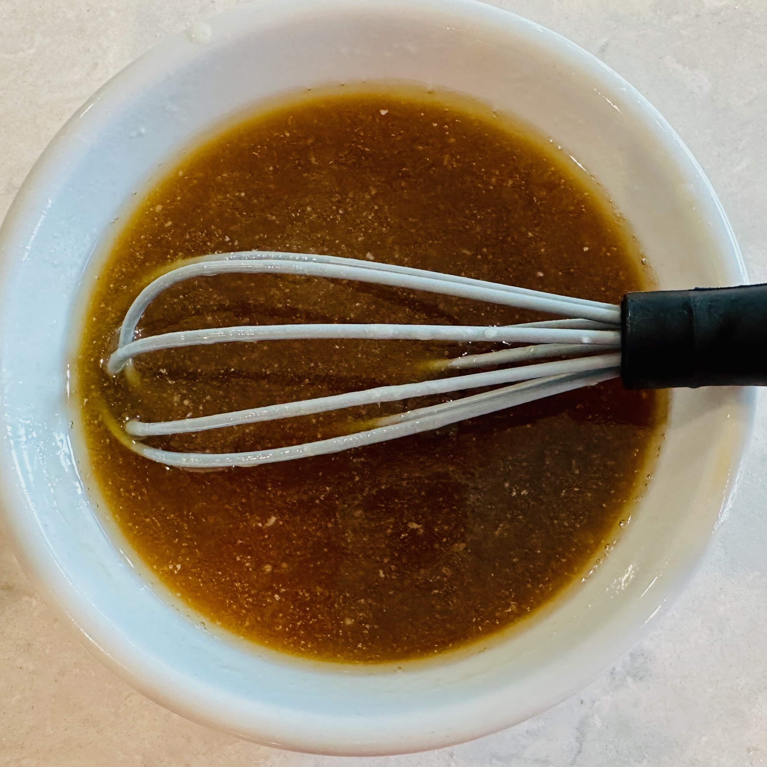 Melted butter and maple syrup mixture in a bowl with a whisk to make sticky buns.