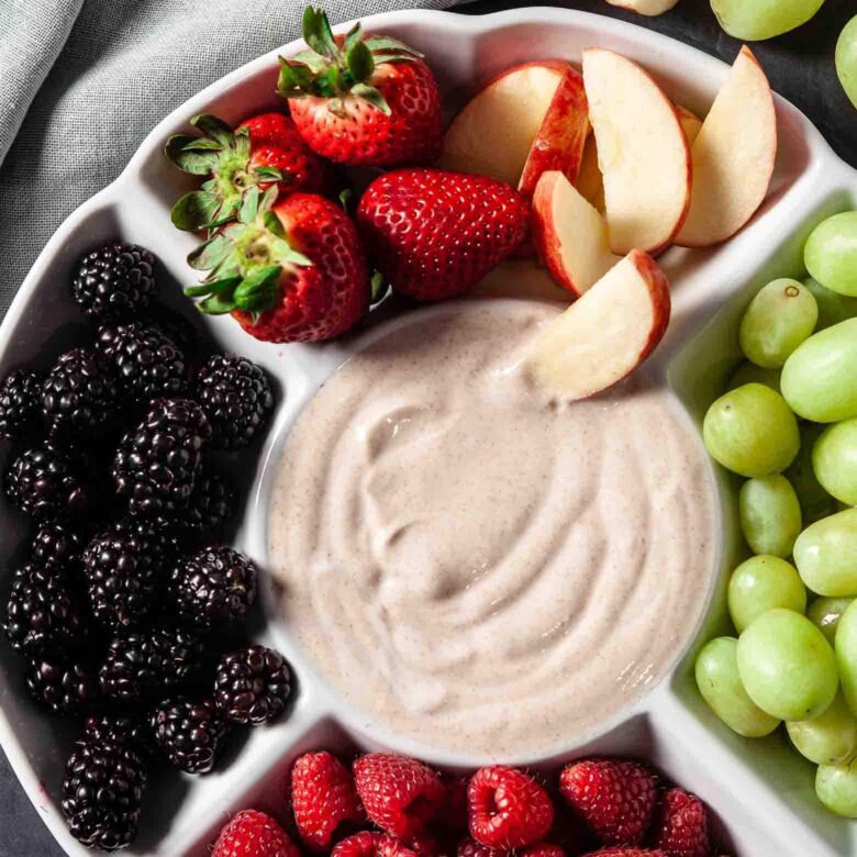 A white plate filled with fruit and dip.