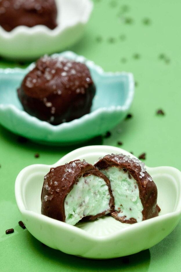 Chocolate-covered mint ice cream balls with sprinkles, one cut in half to show the inside.