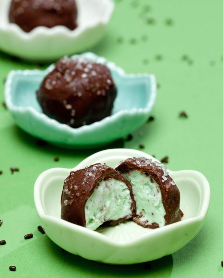 Chocolate-covered mint ice cream balls with sprinkles, one cut in half to show the inside.