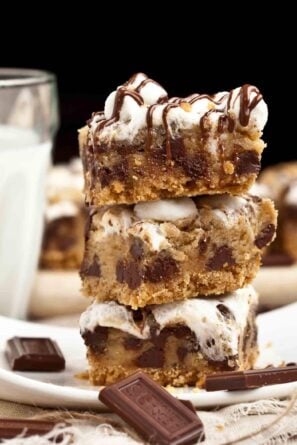 A stack of s'mores cookie bars on a plate with a glass of milk.