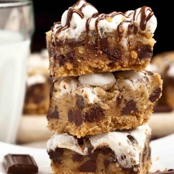 A stack of s'mores cookie bars on a plate with a glass of milk.