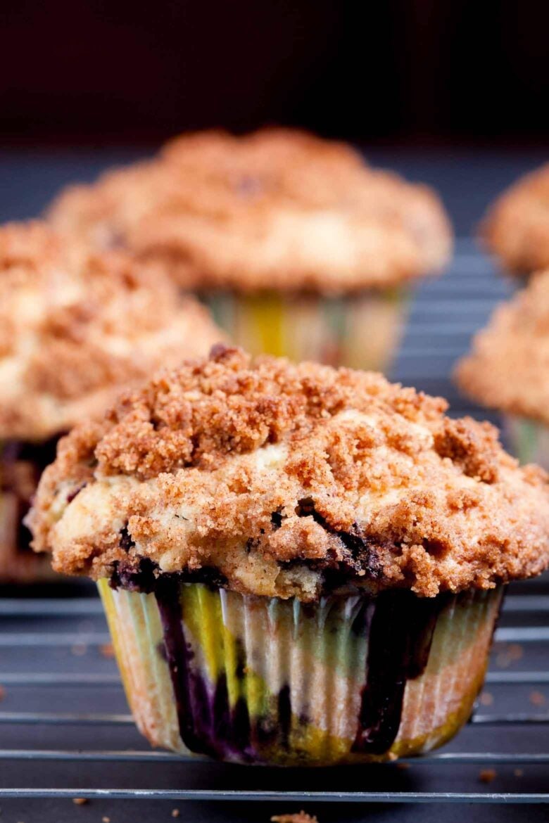 Close-up of blueberry muffins with crumb topping on a dark tray.