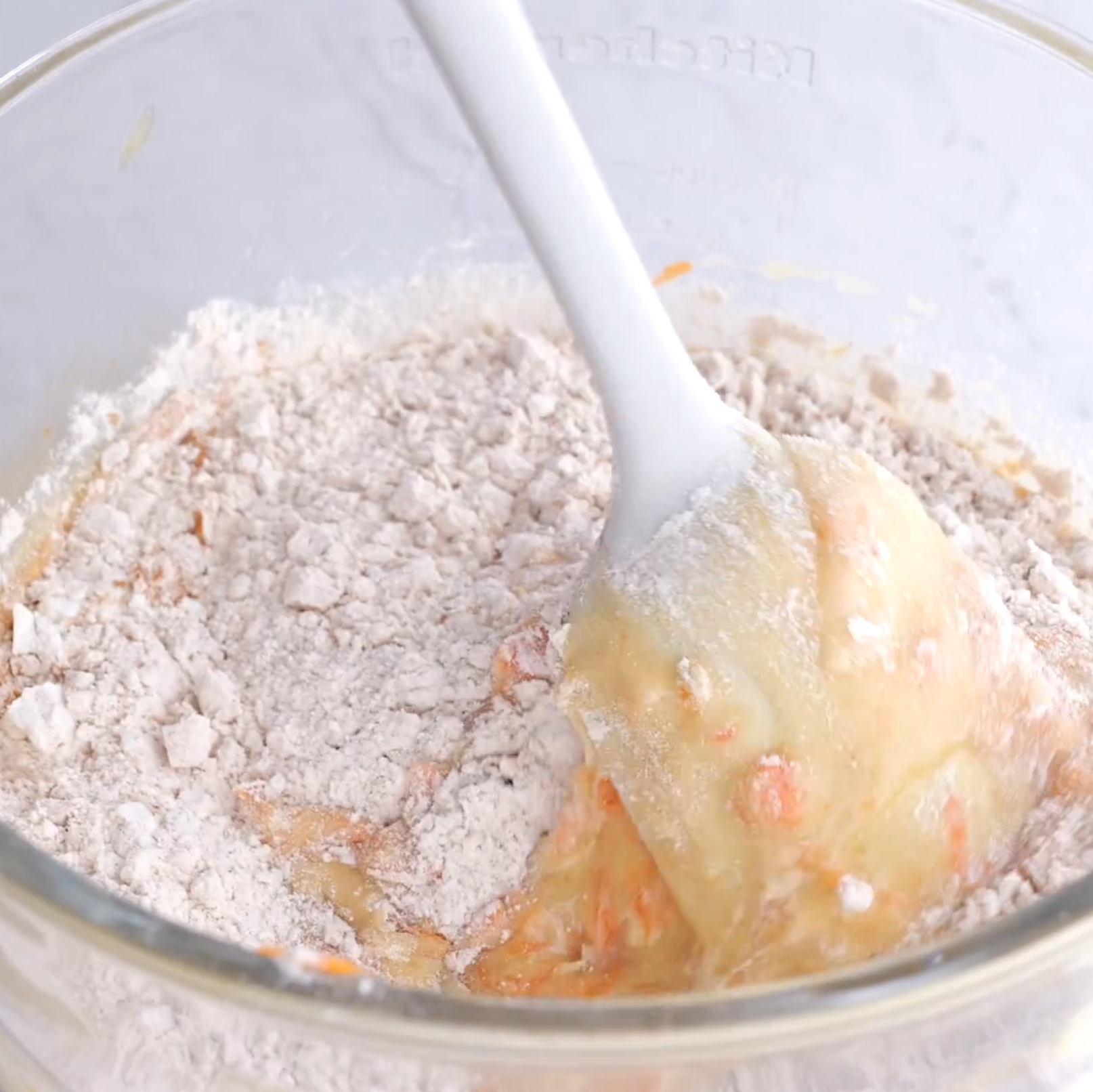 Dry ingredients being folded into wet ingredients containing carrots to make carrot cake.