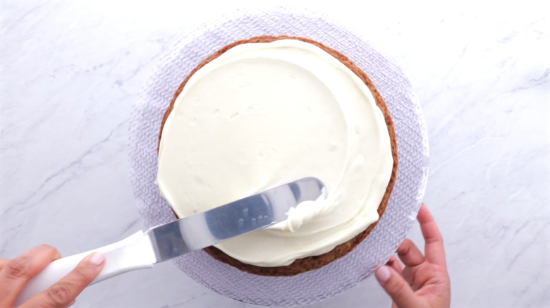 Cream cheese frosting being spread on top of a carrot cake.