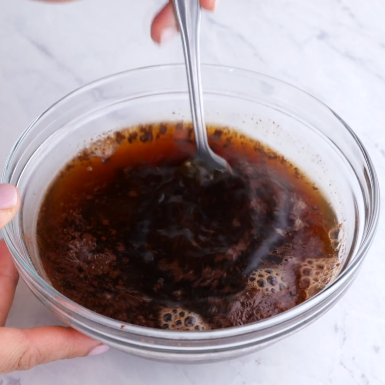 Chopped chocolate being mixed with hot coffee in a glass bowl.