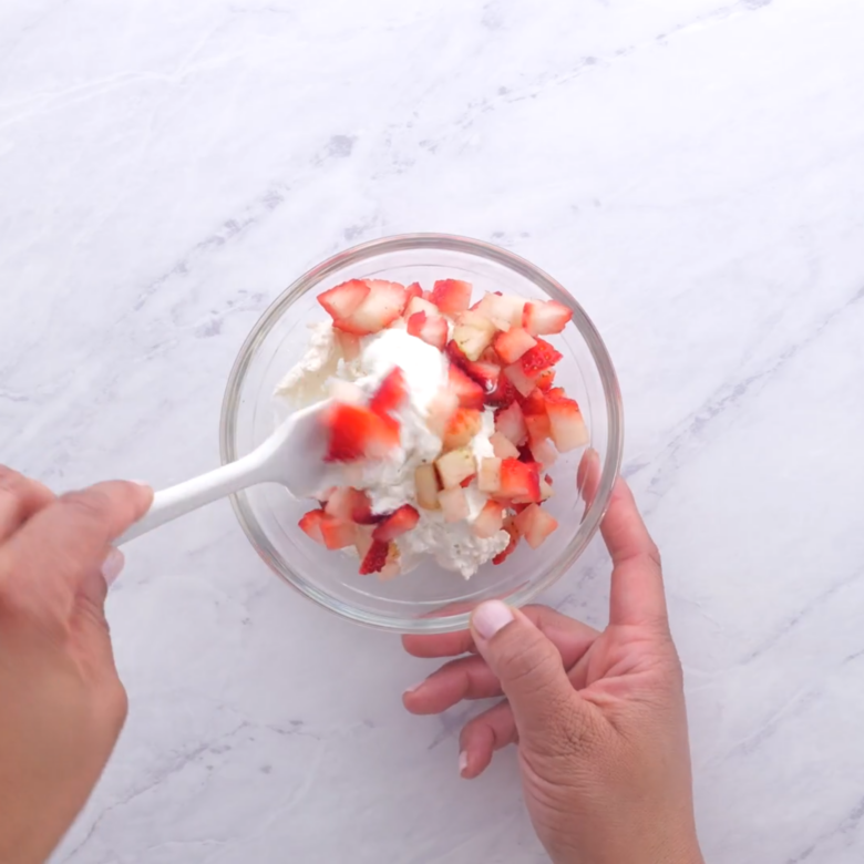 Whipped cream being mixed with chopped strawberries.