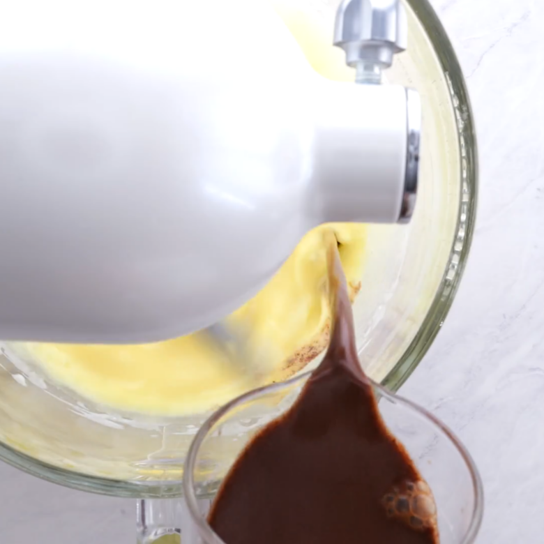 Melted chocolate mixture being added into a bowl with beaten eggs.