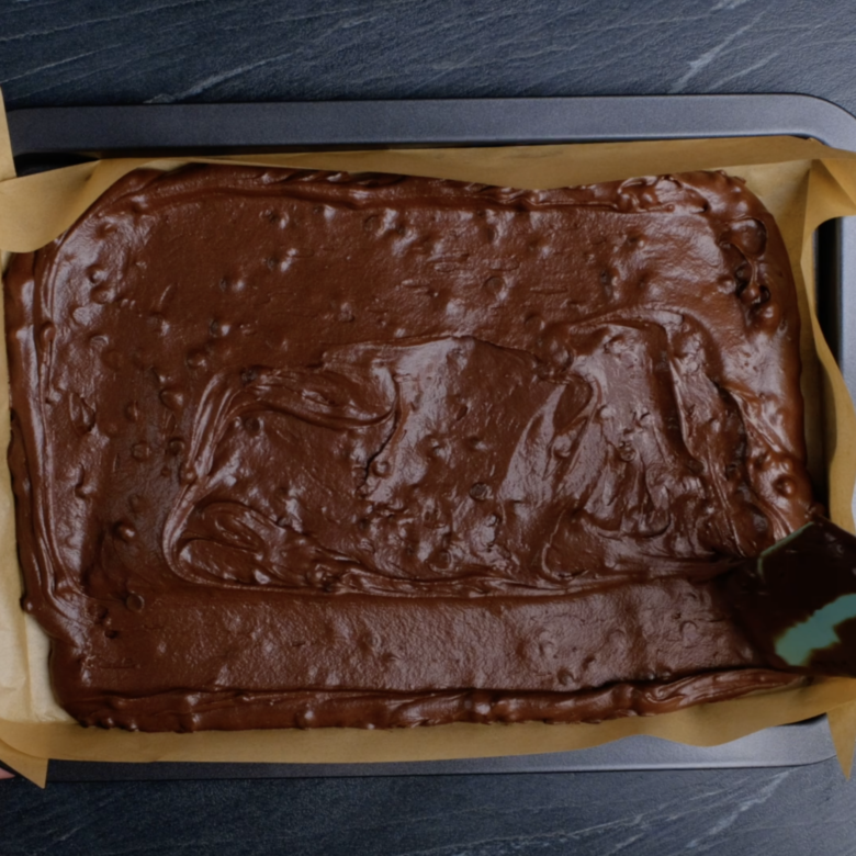 Dark chocolate brownie with chocolate chips batter in a prepared pan, ready to bake.