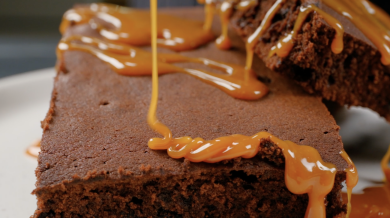 Salted caramel sauce being drizzled on top of dark chocolate brownie pieces.