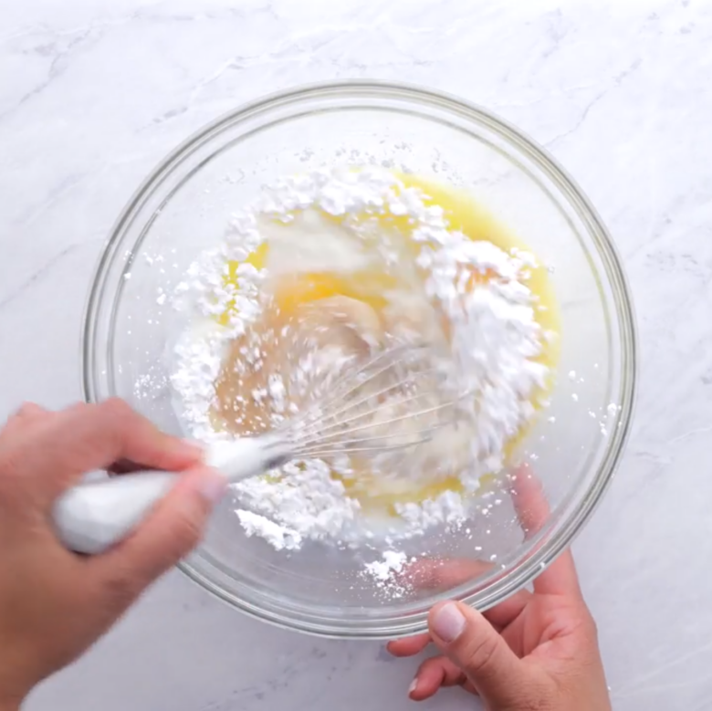 Whisking ingredients to make crepes in a glass bowl on a marble surface.
