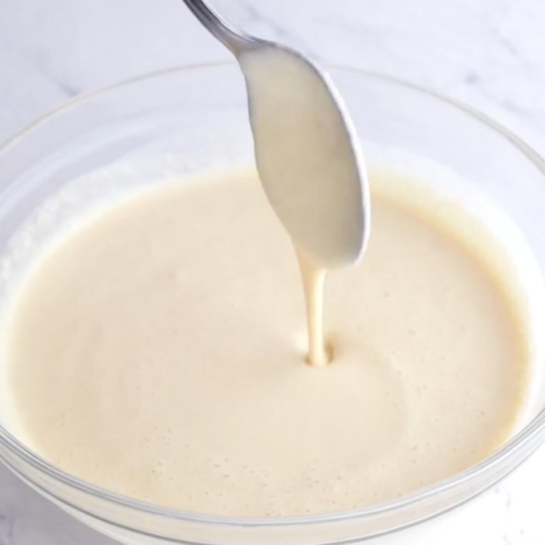 Pouring a smooth, creamy batter from a spoon into a glass bowl.
