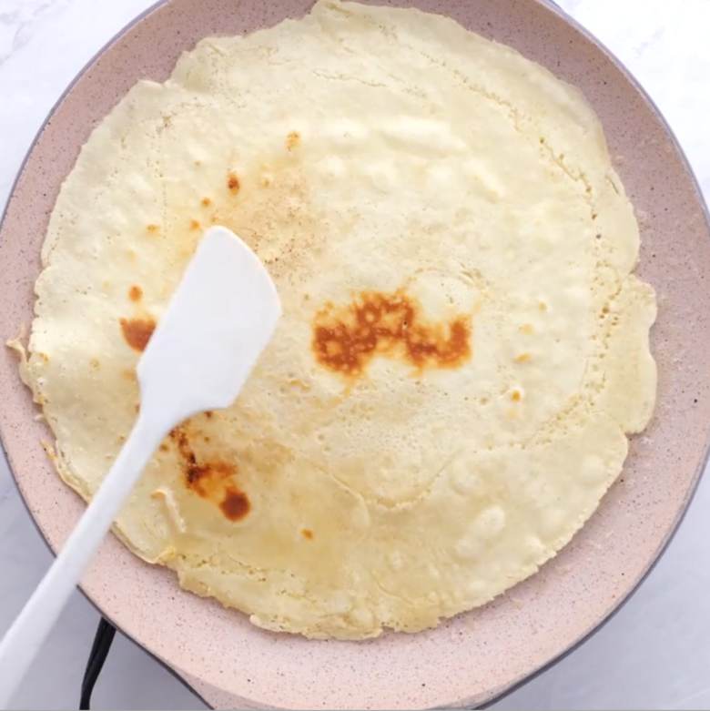 Golden-brown crepe in a frying pan with a spatula.
