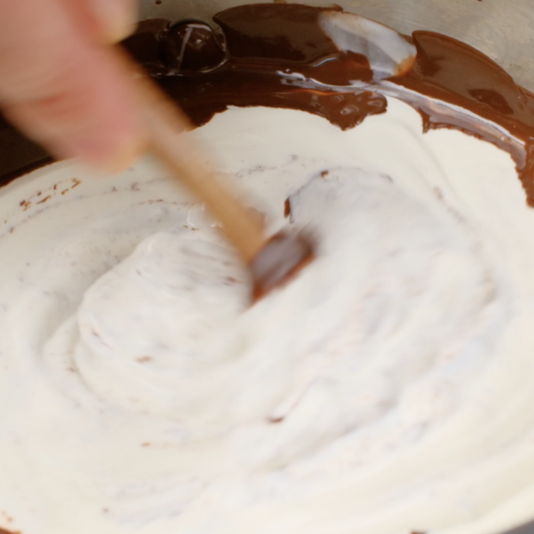 Sour cream being mixed in melted bittersweet chocolate.