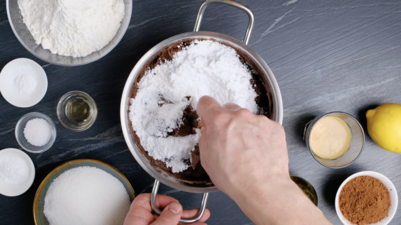 Powdered sugar and salt being mixed into melted chocolate mixture to make eggless chocolate cake.