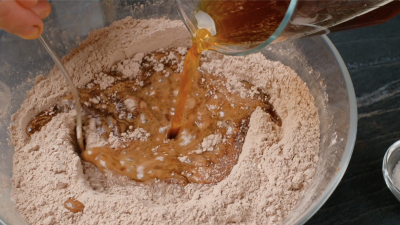 Wet ingredients being incorporated into dry ingredients to make eggless chocolate cake.