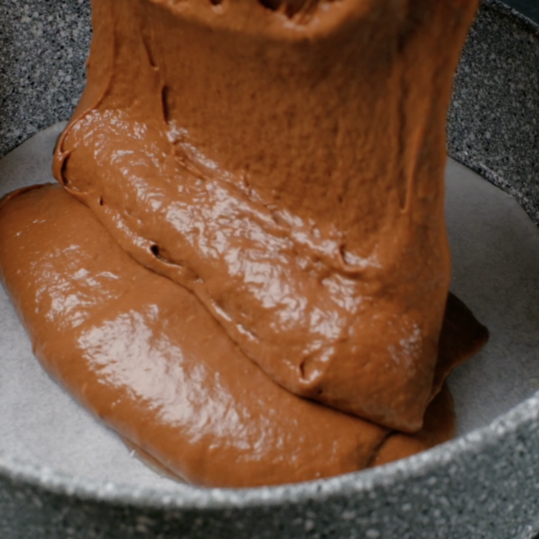 Eggless chocolate cake batter being poured into a prepared cake pan.