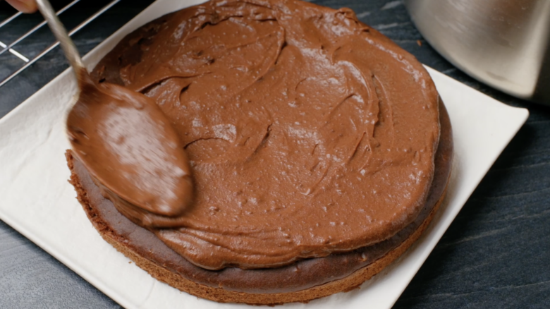 Baked eggless chocolate bake being covered with homemade frosting.