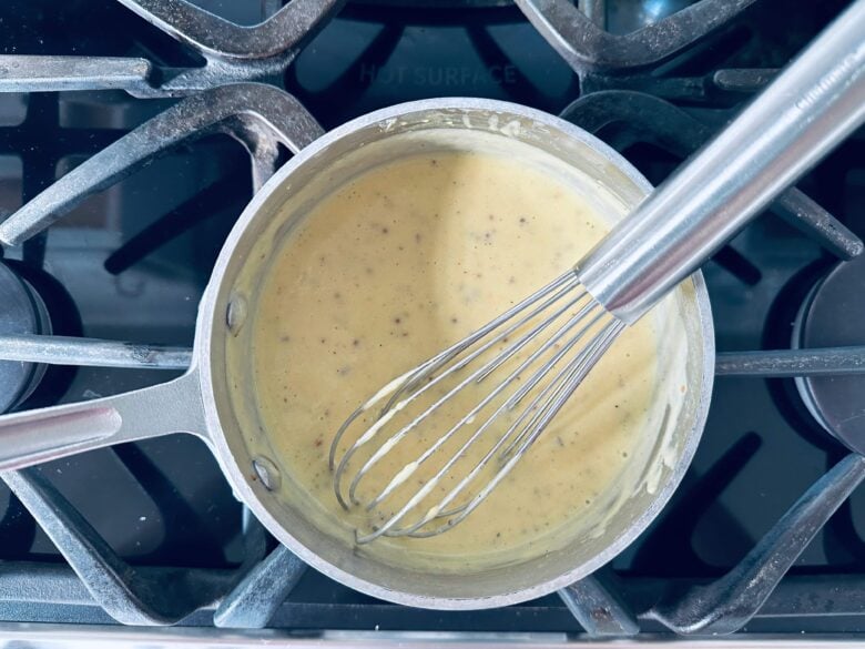 Hollandaise sauce being whisked and made in a small pot over the stovetop.