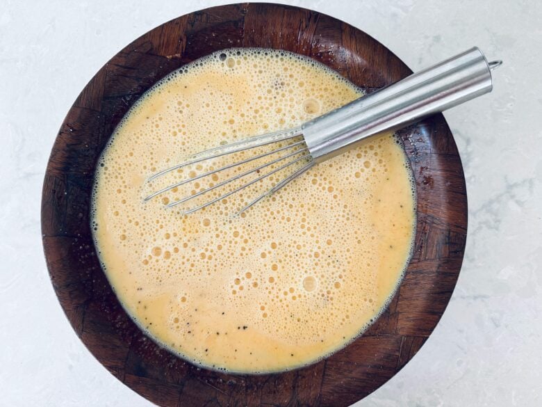 A mixing bowl with eggs benedict custard mixture and a whisk.