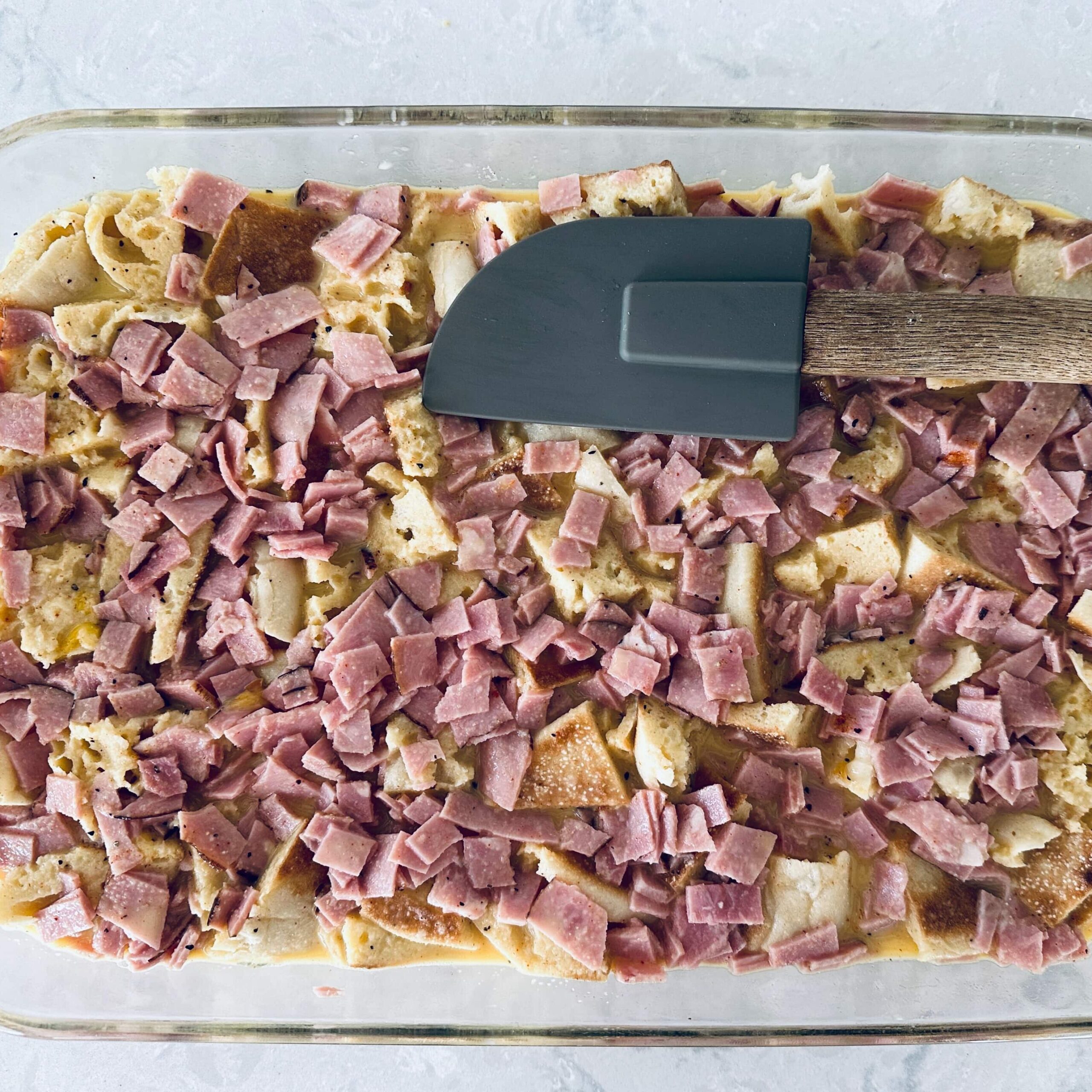 Eggs benedict casserole with custard mixture soaking in it and a spatula on top.