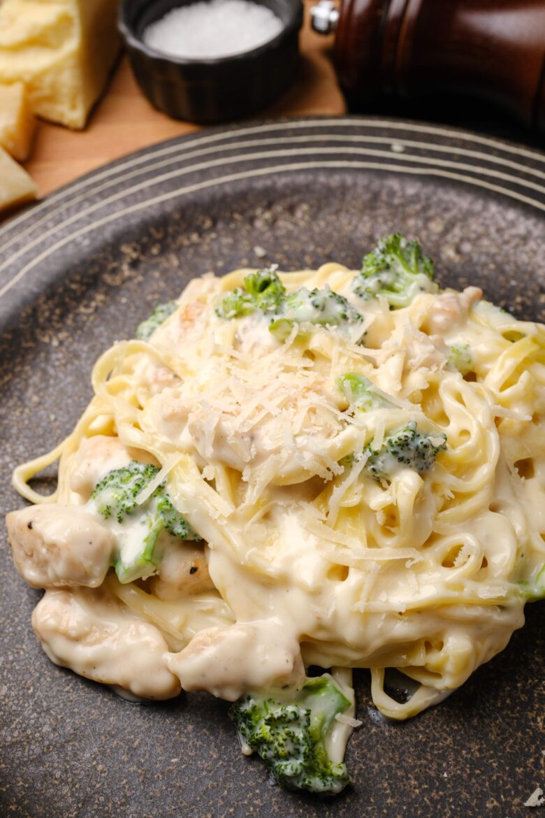 A plate of creamy fettuccini alfredo pasta with chicken and broccoli, topped with grated parmesan cheese.