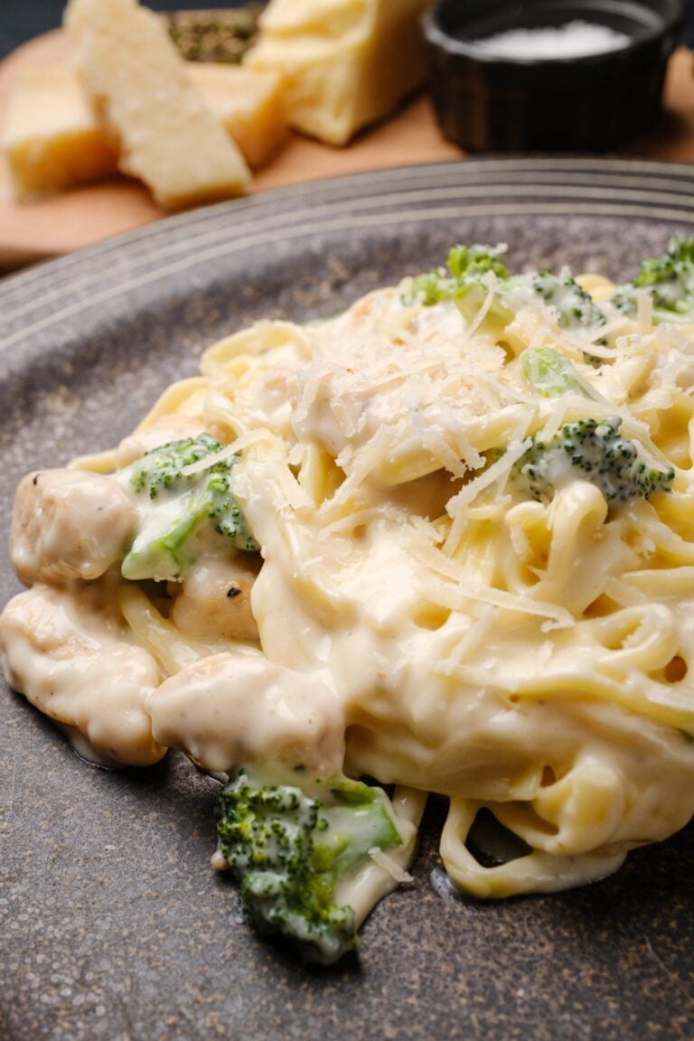 A plate of creamy chicken fettuccini alfredo pasta with broccoli and grated cheese on top, served on a ceramic plate.