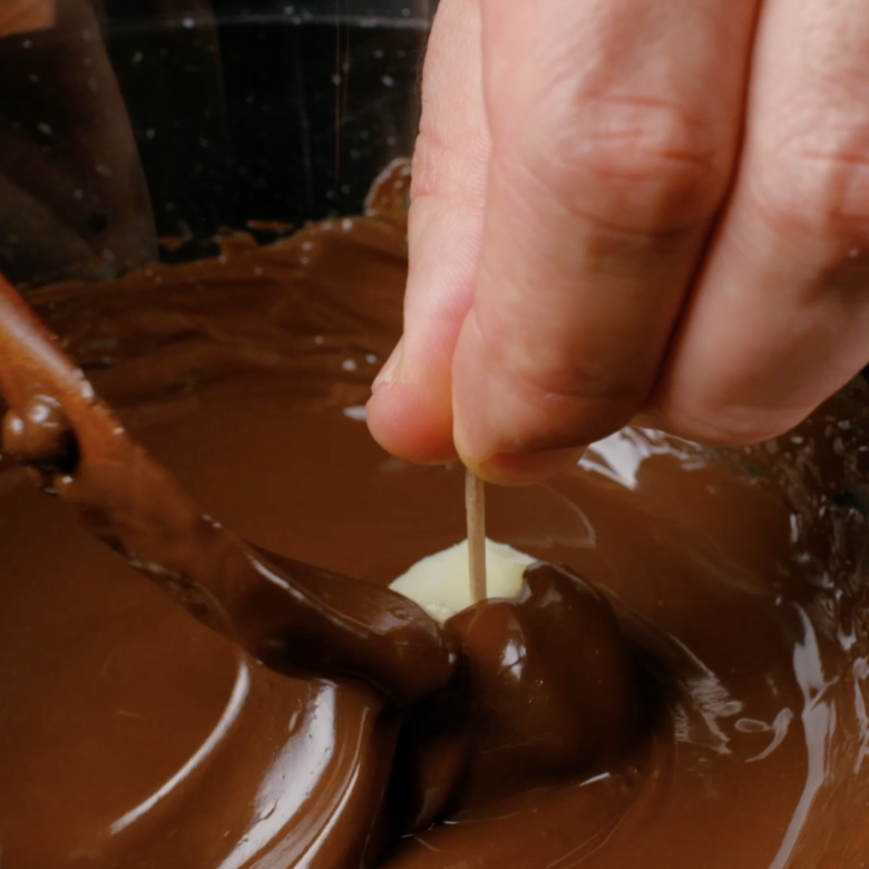 Ice cream balls with tooth being covered with melted chocolate.