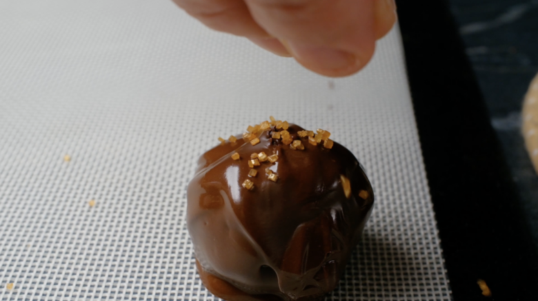 Sugar crystals being sprinkled over chocolate covered ice cream balls before the chocolate sets.