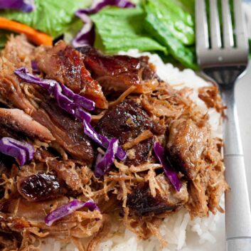 A plate of Hawaiian Kahlua pork over white rice, garnished with red cabbage, carrots, and a side of green lettuce.