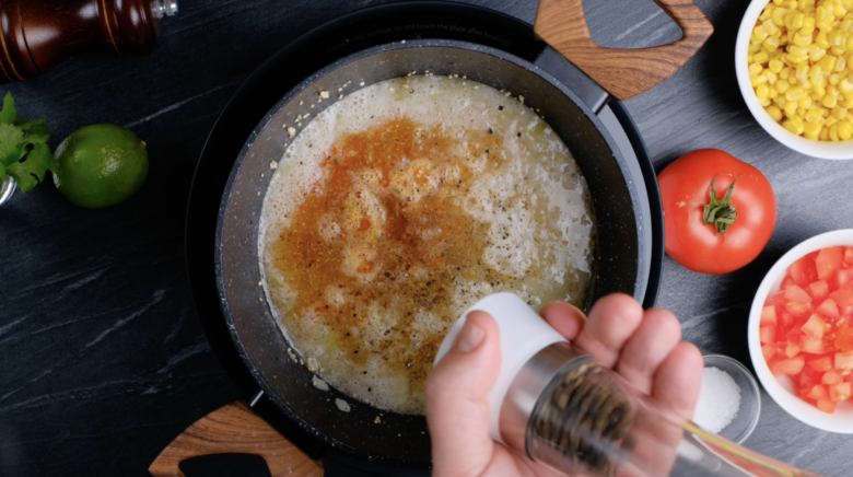 Black pepper and spices being added to a pot with a broth and quinoa mixture.