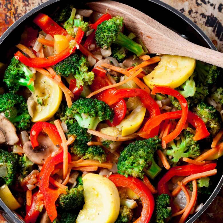 Overhead closeup shot of primavera veggies in a skillet with a wooden spoon.